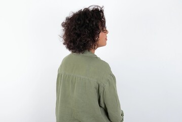 Fototapeta na wymiar The back side view of a young beautiful woman with curly short hair wearing green overshirt over white wall. Studio Shoot.