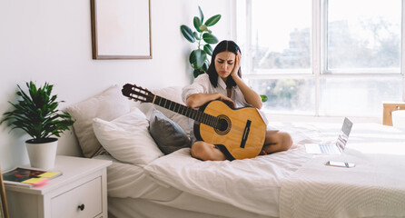Upset brunette female is sad that she can't play guitar. Young woman can’t do hobby with musical instrument because of headache. Bad mood, depression and apathy