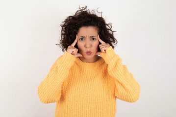 Serious concentrated young beautiful woman with curly short hair wearing yellow sweate keeps...