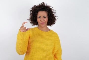 Displeased young beautiful woman with curly short hair wearing yellow sweater over white background...