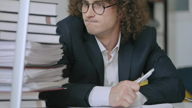 Nerdy man in business suit writing, receiving pile of papers, exhausted by work