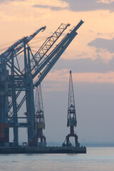 Sea cargo cranes in the port and container terminal of Lisbon, silhouette on sunrise