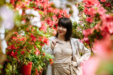 Naklejka premium A girl in a light brown dress and glasses in a garden of blooming azaleas