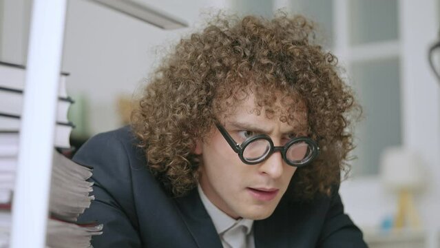 Comic curly male accountant in nerdy eyeglasses shocked by financial report