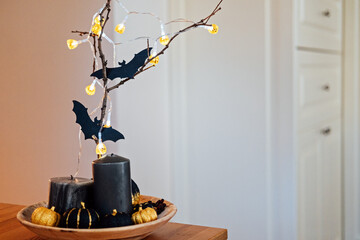 Indoor Halloween decor with black pumpkins, paper bat and light garlands. Dark home interior decorated for Halloween pumpkins, candles and bats on table.