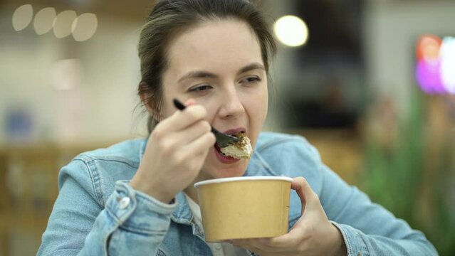 A young girl eats fresh salad from a paper container during her lunch break