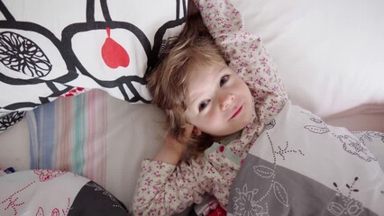 The portrait of a little blonde girl stretching and yawning after waking up. The morning wakening of a healthy cheerful child. A happy kid lying in a cozy warm bed.