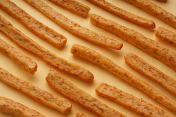 Symmetrical background of appetizing grissini with cheese and sesame on a yellow background, top view