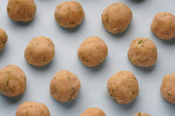 Fototapeta premium Small raw frozen meatballs of light meat on a blue background. Semi-finished products for homemade meatballs and soup