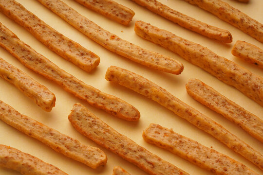 Symmetrical background of appetizing grissini with cheese and sesame on a yellow background, top view