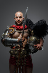 Fototapeta premium Shot of powerful antique gladiator dressed in armor holding plumed helmet and long spear.