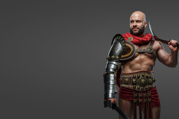 Shot of roman gladiator from ancient rome dressed in armor and cloak against gray background.