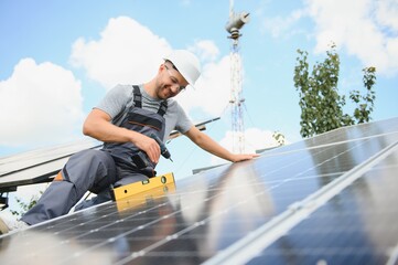 Male engineer in protective helmet installing solar photovoltaic panel system. Alternative energy ecological concept.