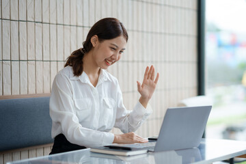 Beautiful Asian businesswoman is video chatting with customer using laptop in office and negotiating gestures smiling and happy face.