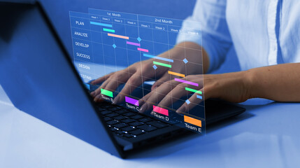 Business Project Management System. Project manager working on laptop and updating tasks and milestones progress planning with Gantt chart scheduling interface for company on virtual screen. 