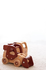 Selective focus on wooden cars truck and bulldozer in natural colors on a white cotton carpet. Environmentally friendly, plastic free toys for toddler. Eco concept. Space for text. Vertical