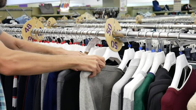 A row of many pullovers hanging on a clothing store rack and a male buyer chooses one