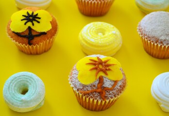 Rows of muffins decorated with powdered sugar and yellow flower shaped icing on a yellow background