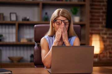 Exhausted woman feels eye fatigue after using laptop. In stress, an overworked woman takes off her...