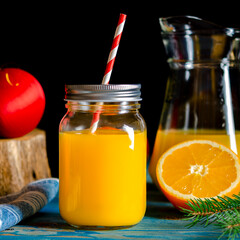 Orange juice in a jar with a straw stands on a wooden table