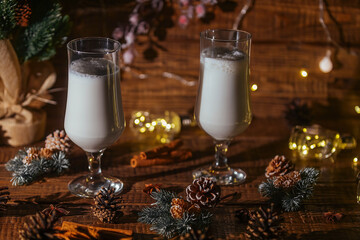 Christmas hot drink Eggnog with cinnamon is poured into two glasses on a wooden background with...