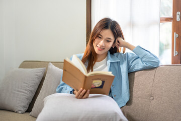 Young woman is reading a book or literature while sitting on comfortable the couch to relaxing