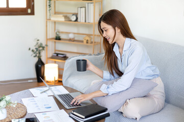 Female freelance is typing information on laptop and drinking coffee while sitting on comfortable