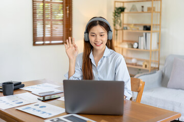 Female freelance is using laptop and wearing headphone to meeting video conference with colleague