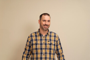 Portrait of Hispanic bearded man dressed in a plaid shirt looking at the camera while smiling,...