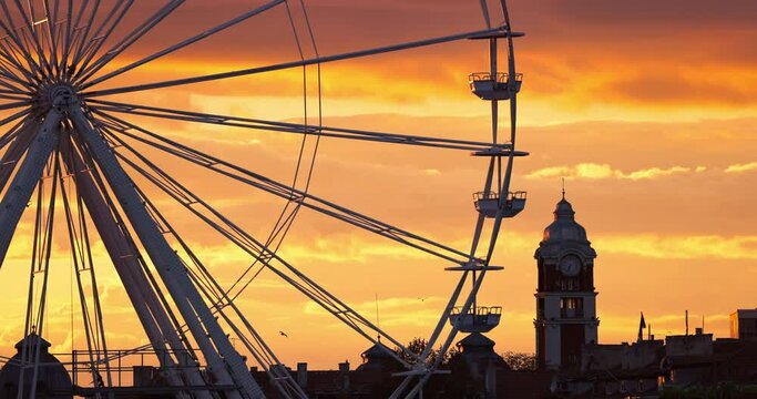 Ferris Wheel in amusement park and scenic sunset clouds in sky and flying birds silhouettes around buildings