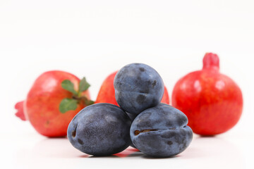 Black plum on a background of ripe pomegranates. Shallow depth of field