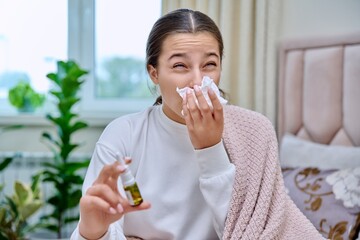 Teenage girl with runny nose treating rhinitis using nose drops spray - obrazy, fototapety, plakaty