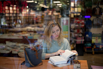 View through the book shop window of young blonde woman reading book.