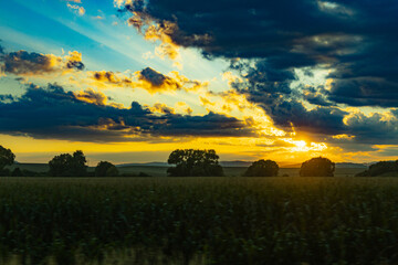 Naklejka premium Beautiful shining sun behind big clouds at sunset over big fields