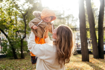 Mother and son walking in autumn park outdoor. Woman holding toddler boy on hands. Family of two