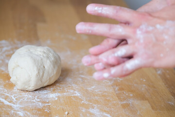 Kneading dough on the wooden table, lump of dough next to a hands in flour