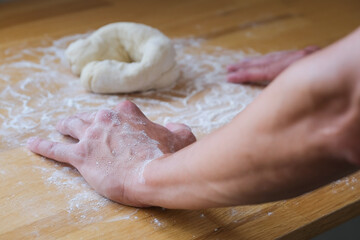 Close up of hands in flour lean on the table next to dough 