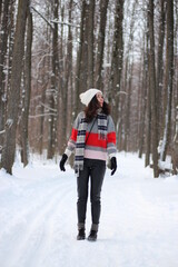 A young woman in a sweater and a white hat in the forest. Full length portrait. Snowing. Winter atmosphere. Walk in the forest.