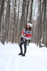 Fototapeta na wymiar A young woman in a sweater and a white hat in the forest. Full length portrait. Snowing. Winter atmosphere. Walk in the forest.