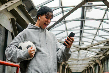 Young hipster man in hoodie and hat holding smartphone and celebrate win a bet on the urban...
