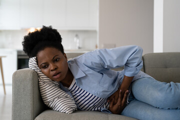 Sick African American woman experiencing health problems suffering from cramps and stomach pain....