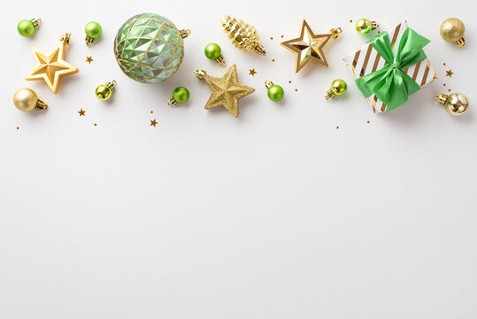 Christmas Eve concept. Top view photo of giftbox with ribbon bow gold green transparent baubles star pine cone ornaments and glowing confetti on isolated white background with copyspace