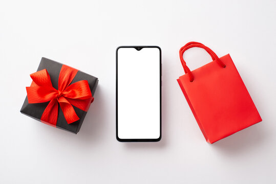 Cyber monday concept. Top view photo of smartphone red paper bag and giftbox with ribbon bow on isolated white background with copyspace