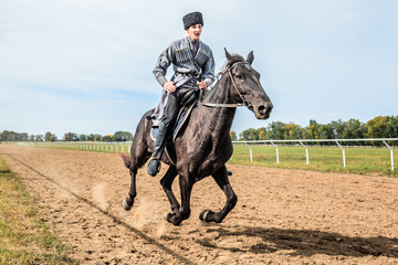 Cossack man in a national costume is galloping rapidly on a black horse around the hippodrome