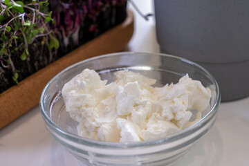 glass bowl with delicious cream on white kitchen table and exhaust kitchen background with greens and gray pot in the background