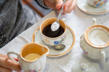 Young man's hands preparing and drinking a coffee with milk and sugar using a vintage porcelain cup with flowers pattern.