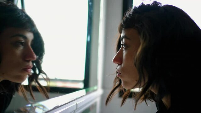 South American woman looking at herself in mirror reflection. A hispanic latin girl standing by bathroom mirror