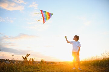 Boy is running with a kite during the day in the field