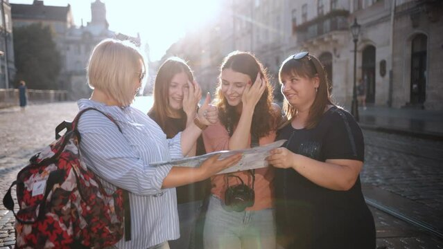 During a hot summer day, a female tour guide explains the tour to tourists while they are looking at a map of the city. Tourists with maps in the old part of the city. Go Everywhere