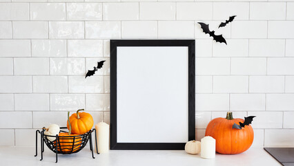 Vertical black picture frame mockup with pumpkins and halloween home decor on white desk table in...
